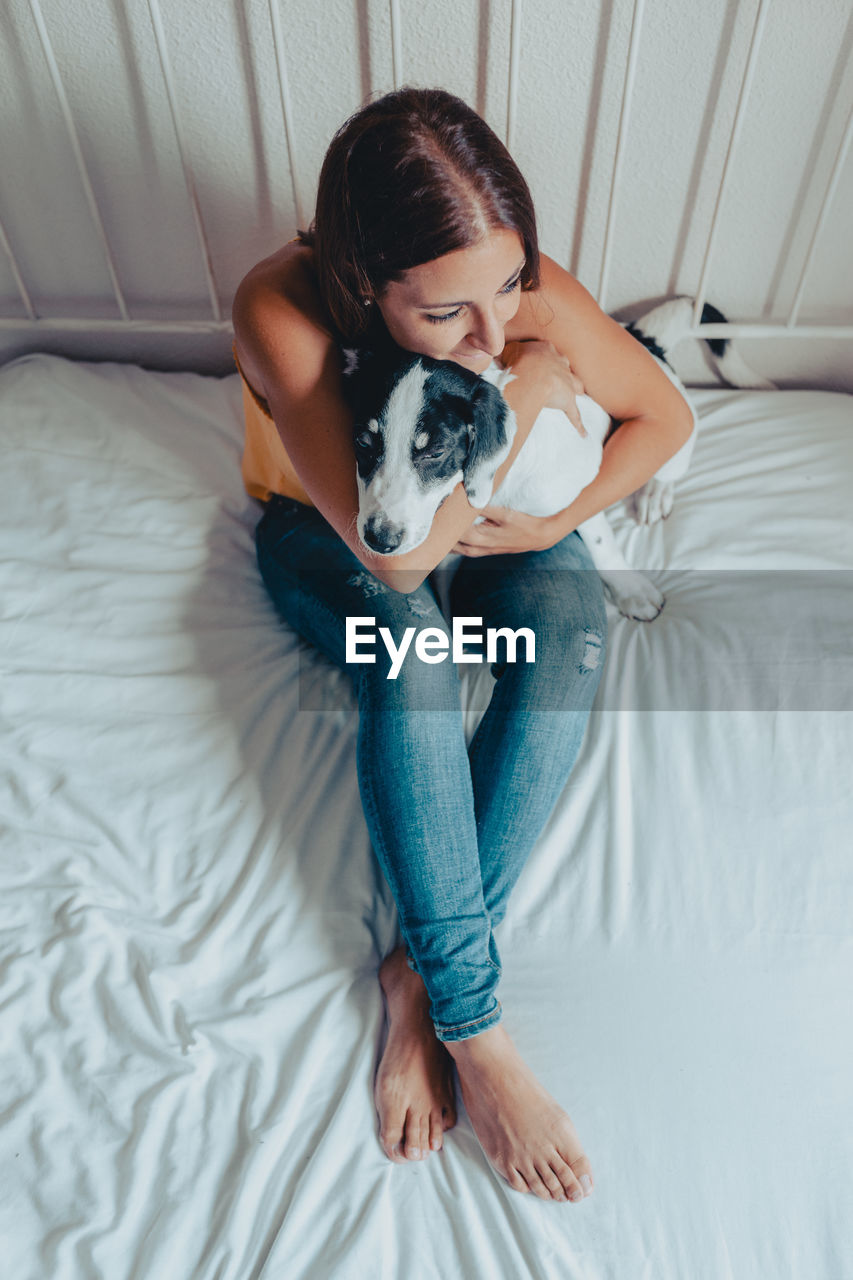 FULL LENGTH OF A YOUNG WOMAN WITH DOG ON BED