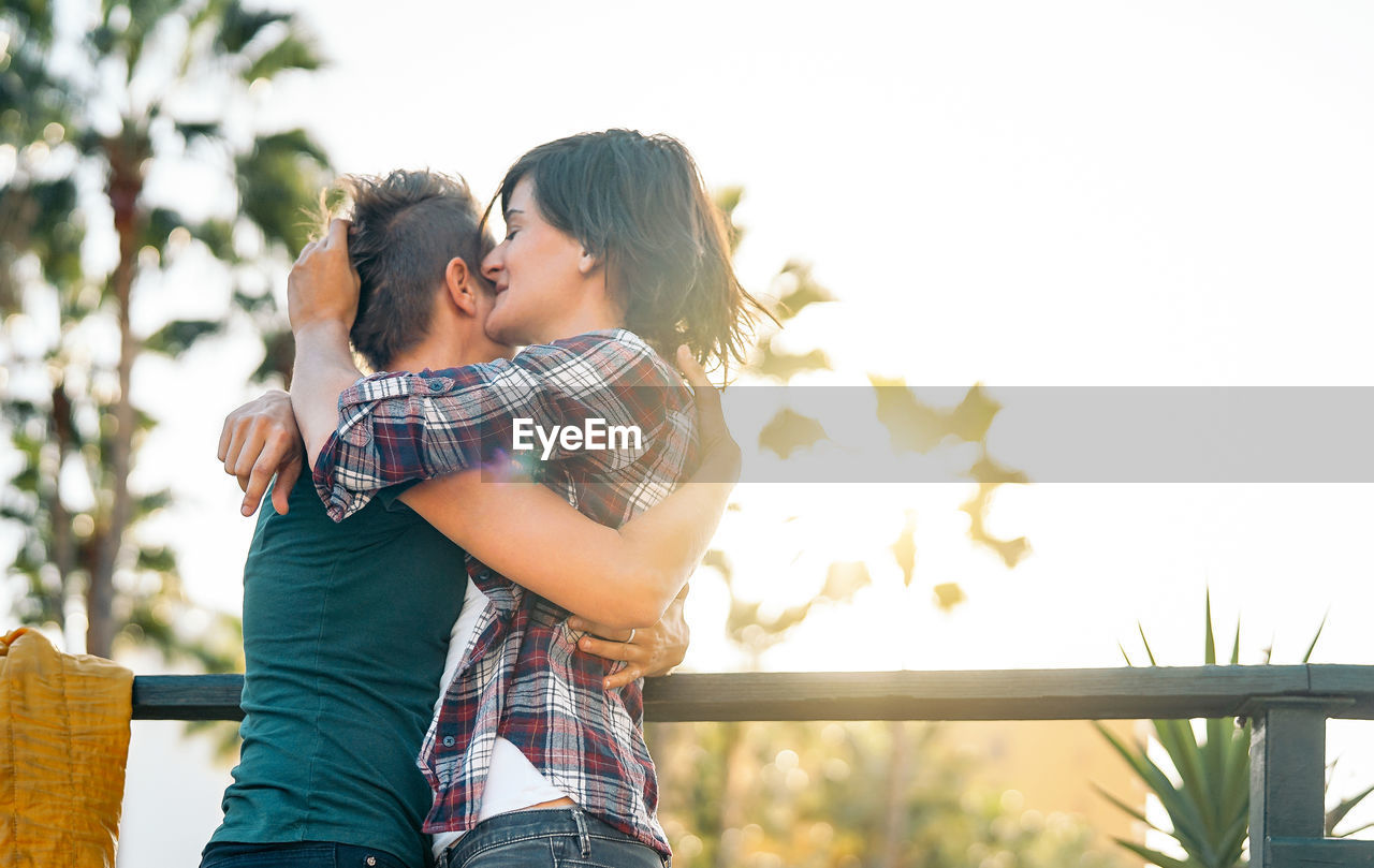 Low angle view of young women embracing by railing against sky