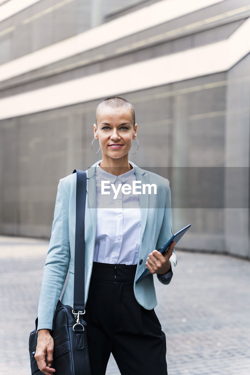 Smiling businesswoman with tablet pc standing on footpath