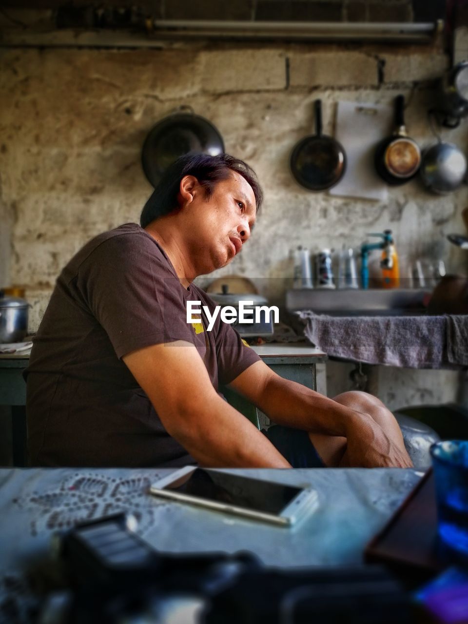 Side view of thoughtful mature man looking away while sitting in kitchen