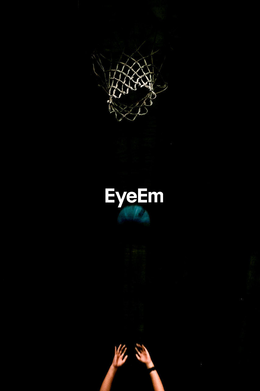 Cropped image of hands throwing basketball into hoop at night