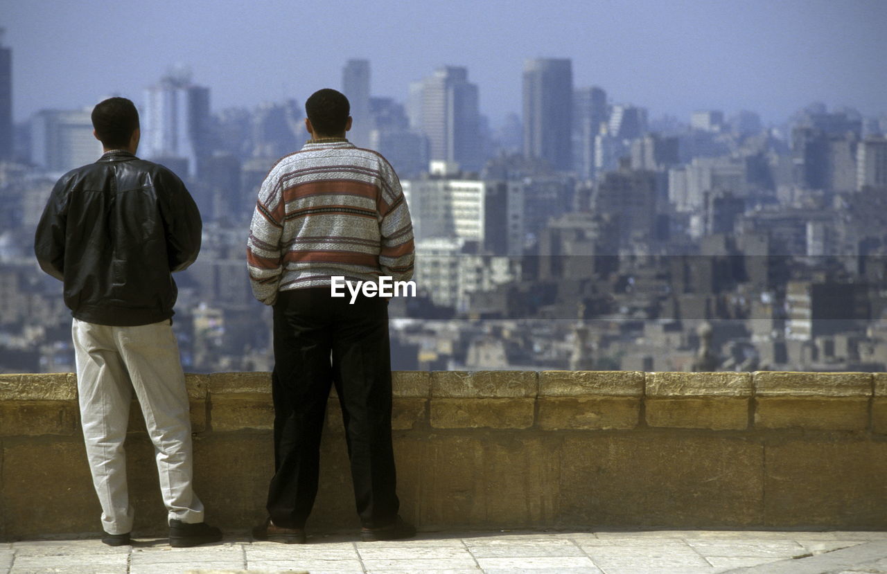 Rear view of men standing by railing against city buildings