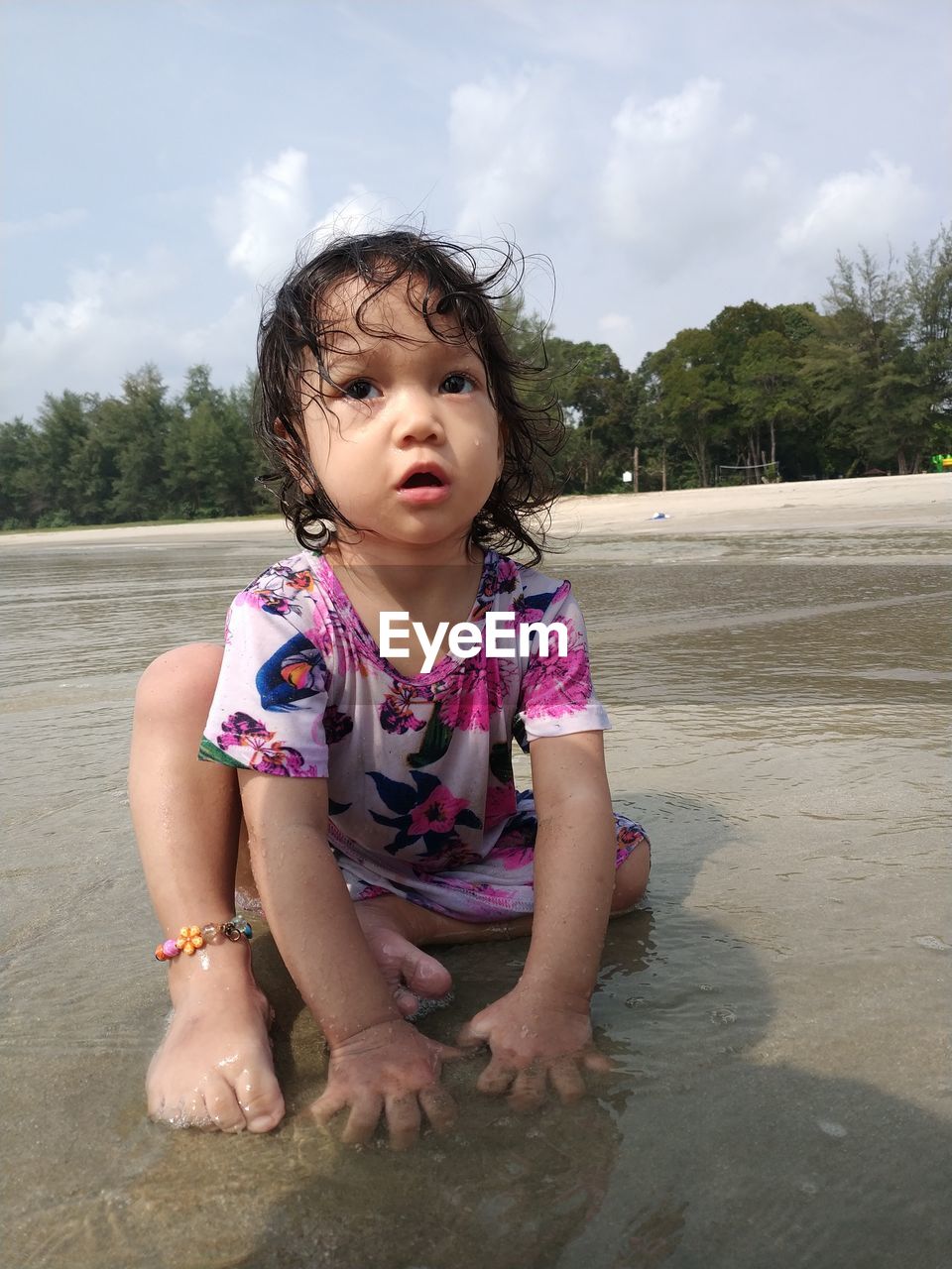 Cute girl sitting in sea against sky