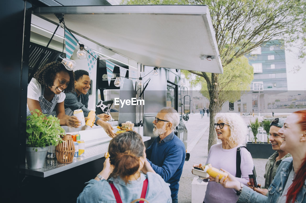 Smiling male and female customers talking to food truck owners in city