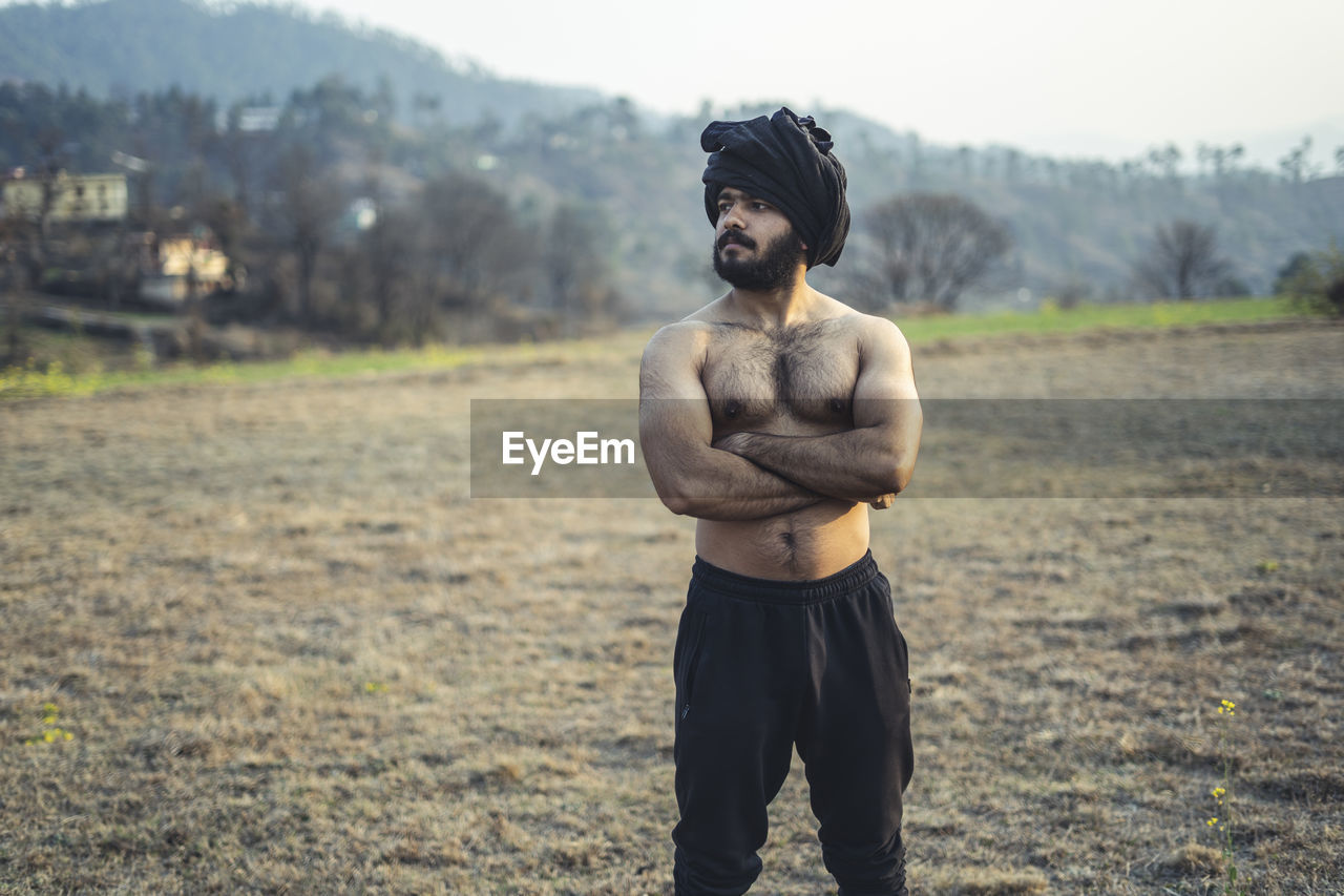 Young indian farmer with a turban standing on a barren field. crops not growing due to shortage