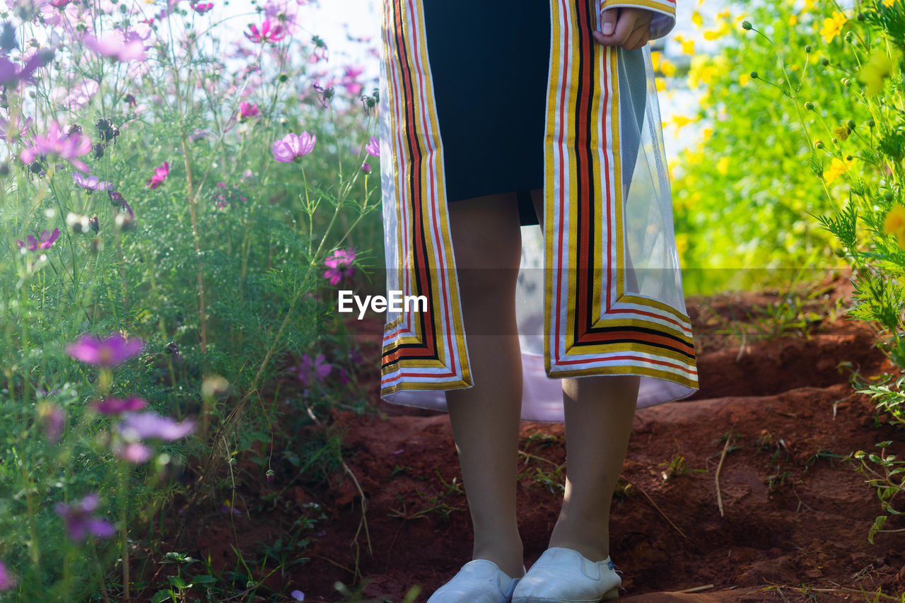 LOW SECTION OF WOMAN STANDING ON FLOWERING PLANTS BY RAILING