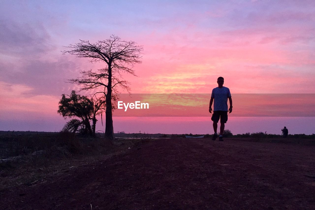 Rear view of silhouette man standing on land against sky during sunset