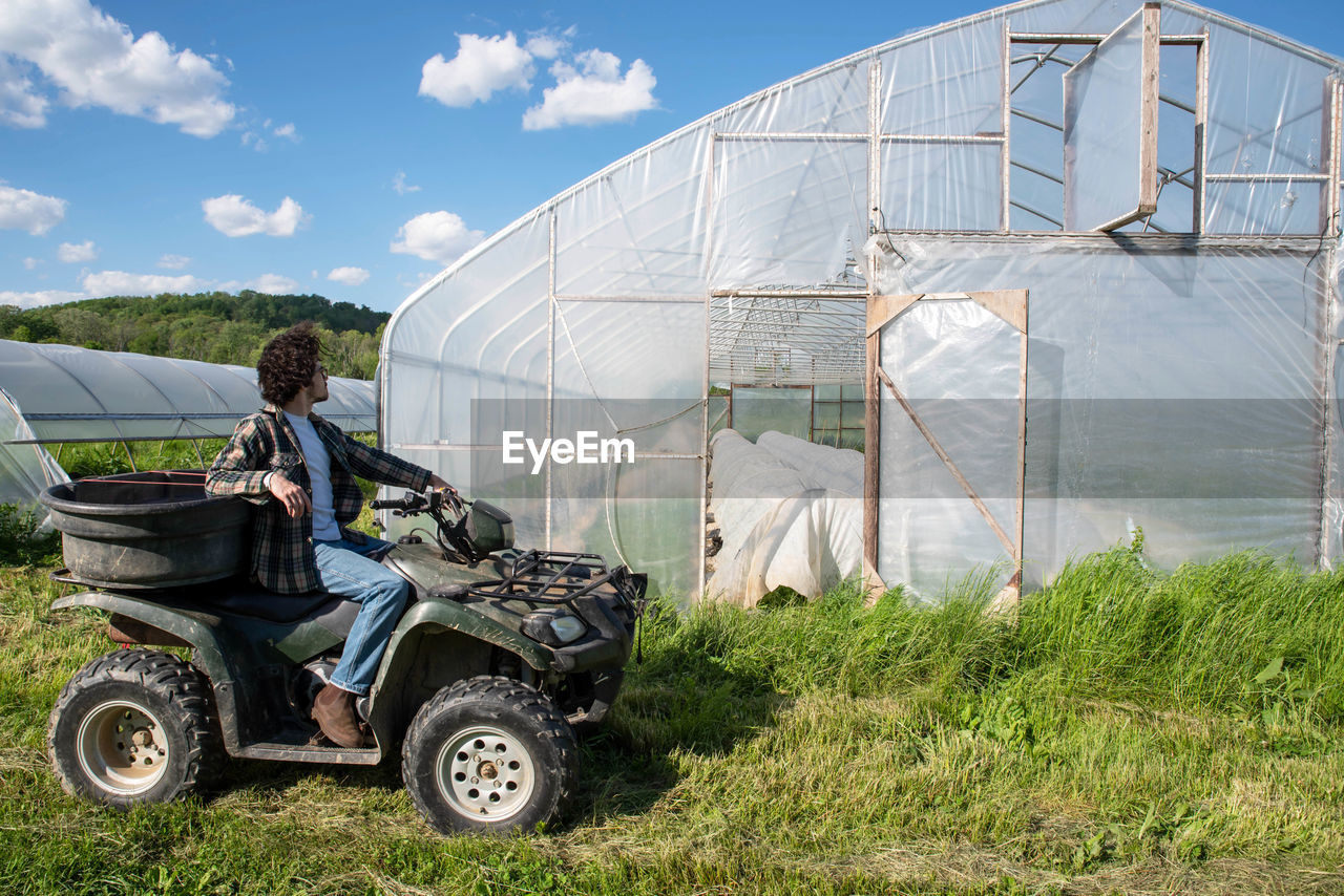 Young farmer on off road vehicle inspects vegetable greenhouse