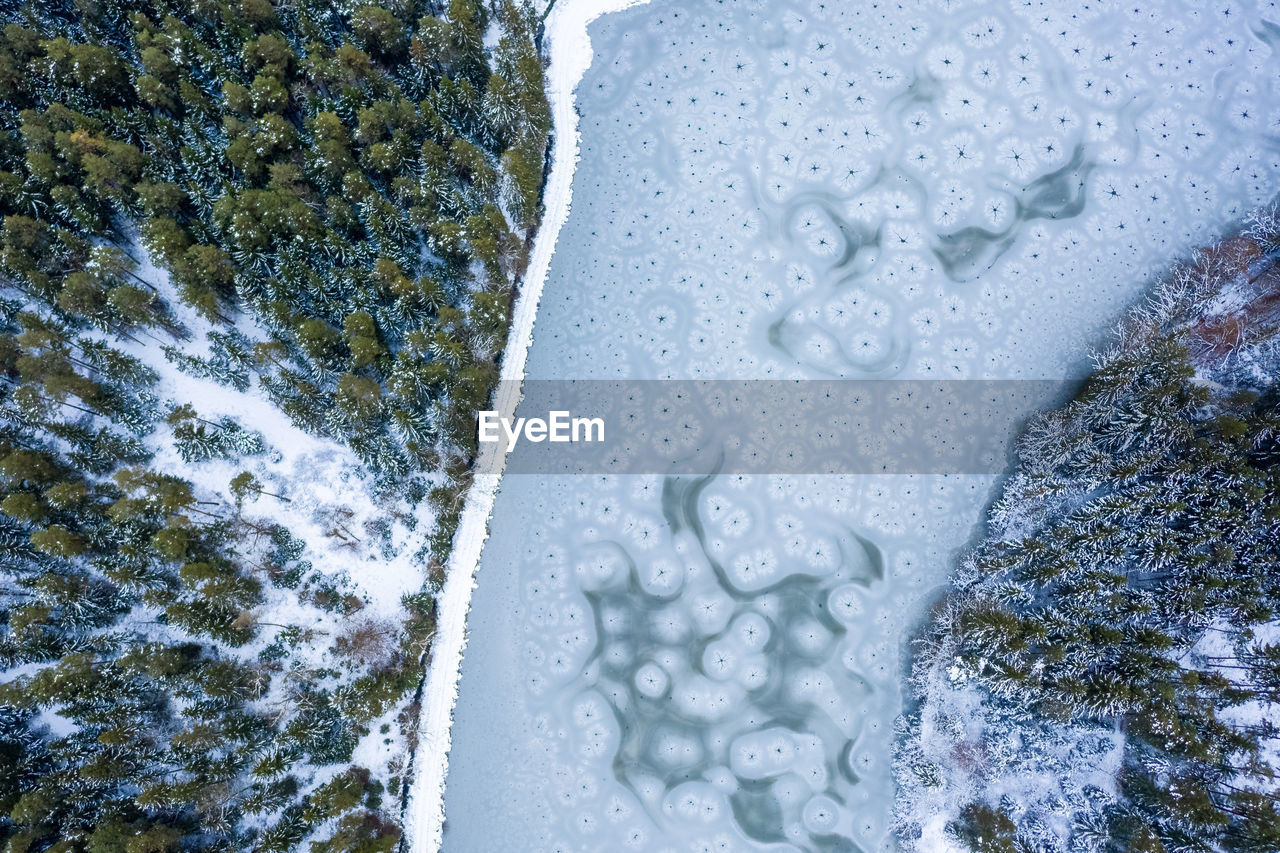Flight over frozen lake in forest, austria. aerial photography during winter season.