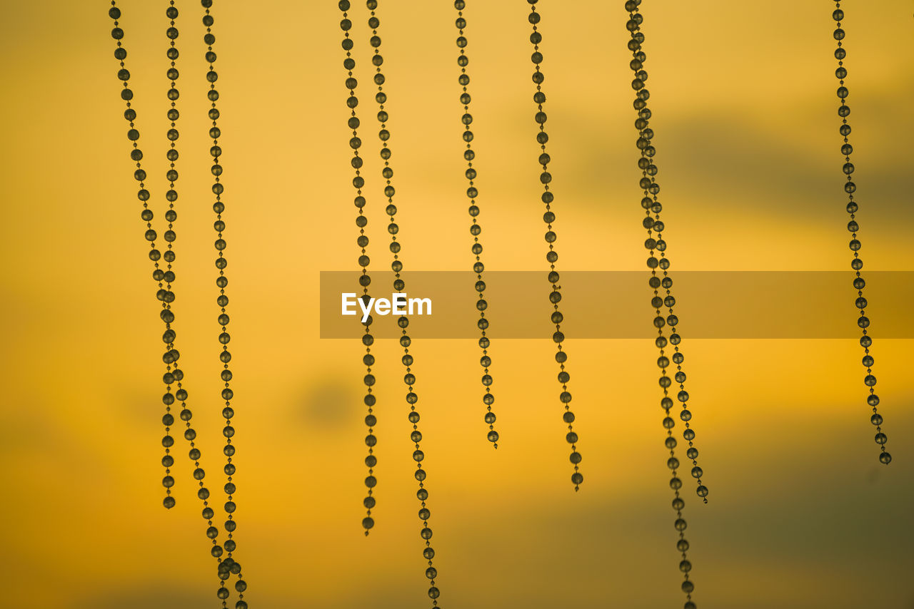 Close-up of beads hanging against orange sky during sunset
