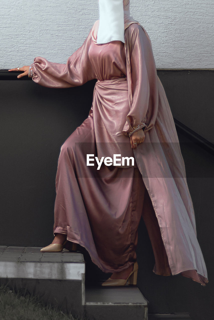 Full length image of veiled woman with white niqab and pink silky dress standing on the stairs