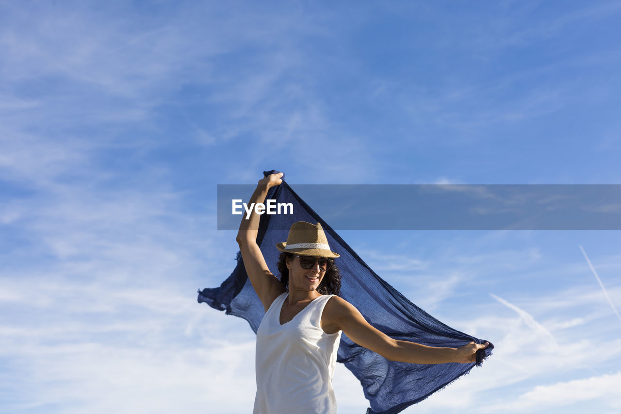 LOW ANGLE VIEW OF WOMAN WITH ARMS RAISED AGAINST SKY