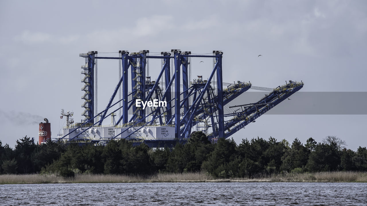 VIEW OF CRANES AT RIVERBANK AGAINST SKY