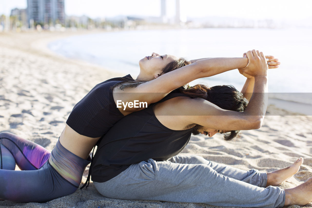 Side view of couple doing yoga together on beach