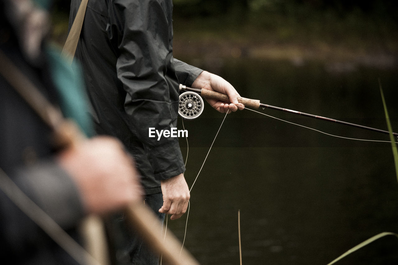 Midsection of man holding fly fishing rod