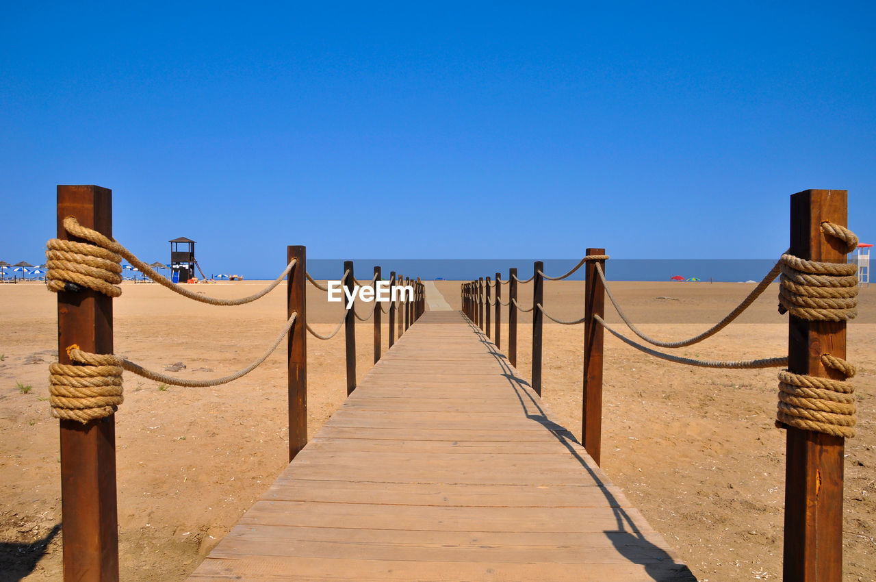 View of wooden walkway against clear blue sky