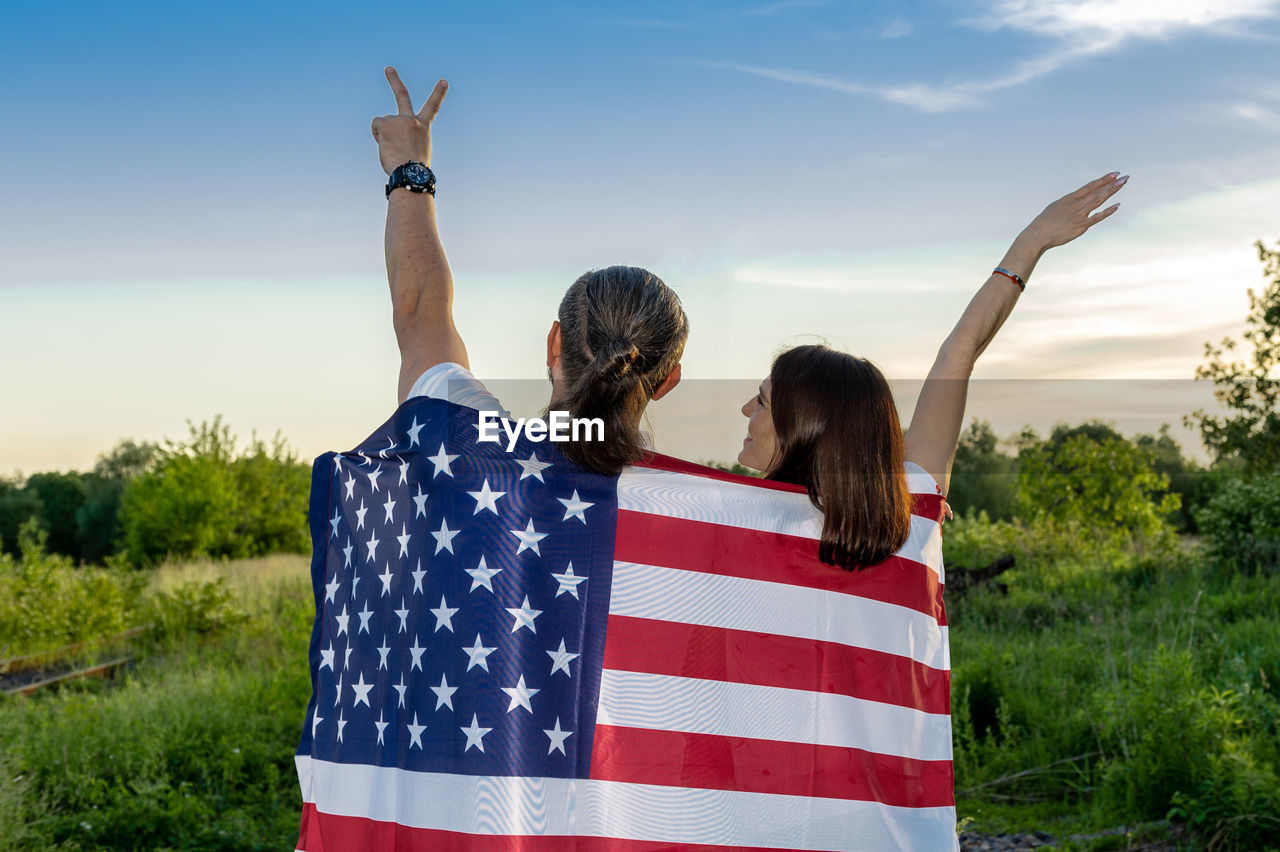 Back view of man and woman holding american flag outdoor.