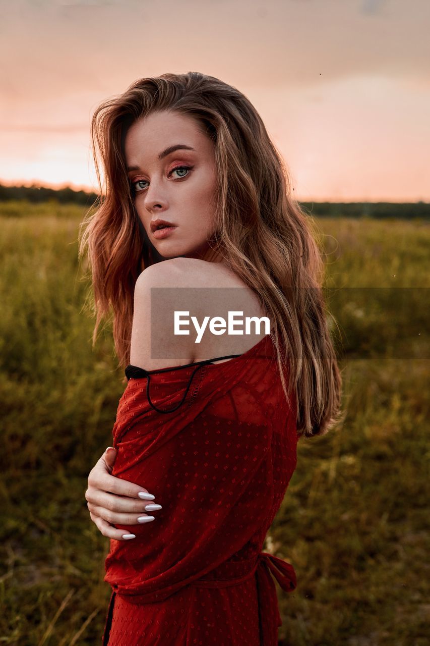 Portrait of beautiful woman standing on land against sky during sunset