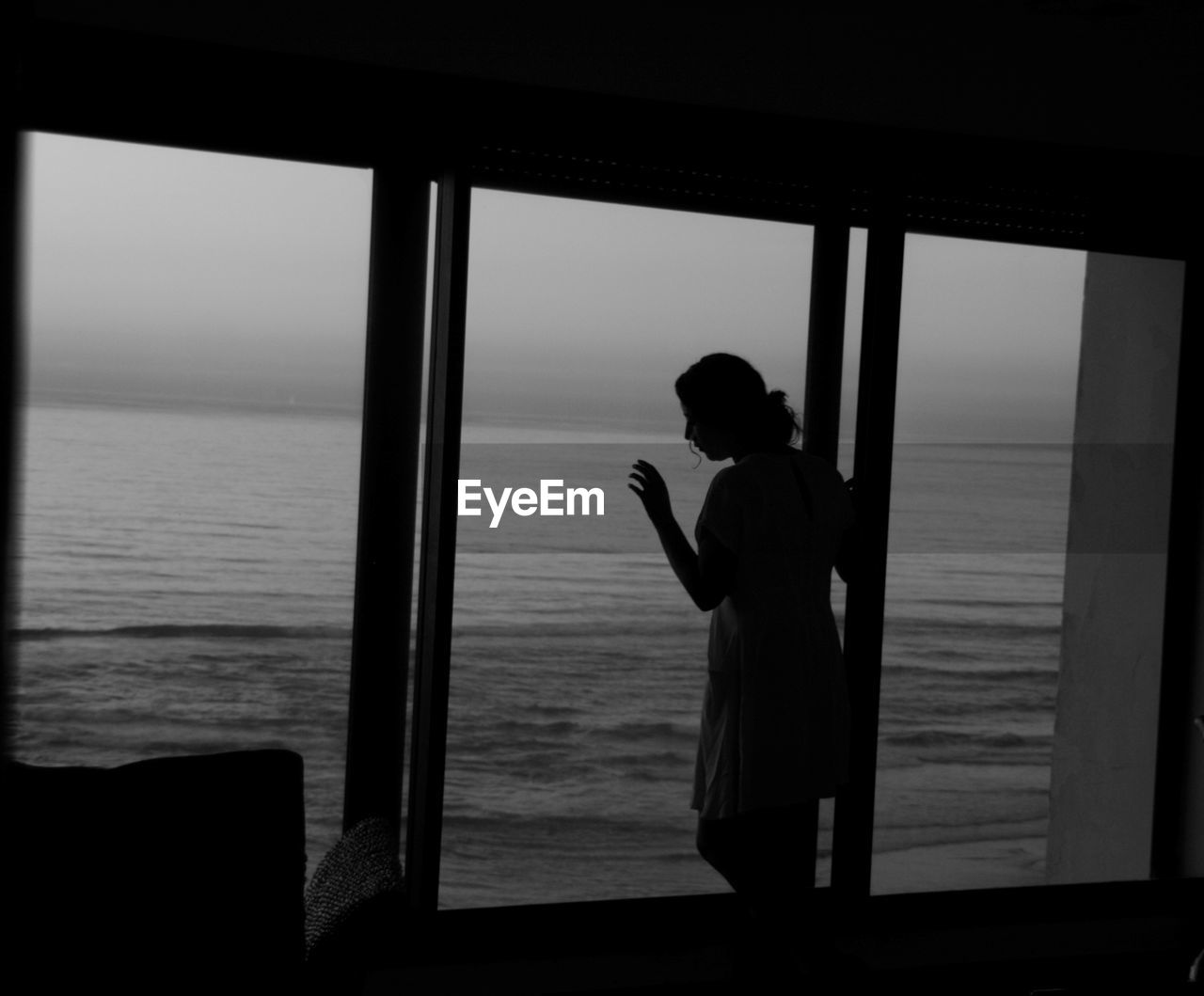 Woman standing at window against sea