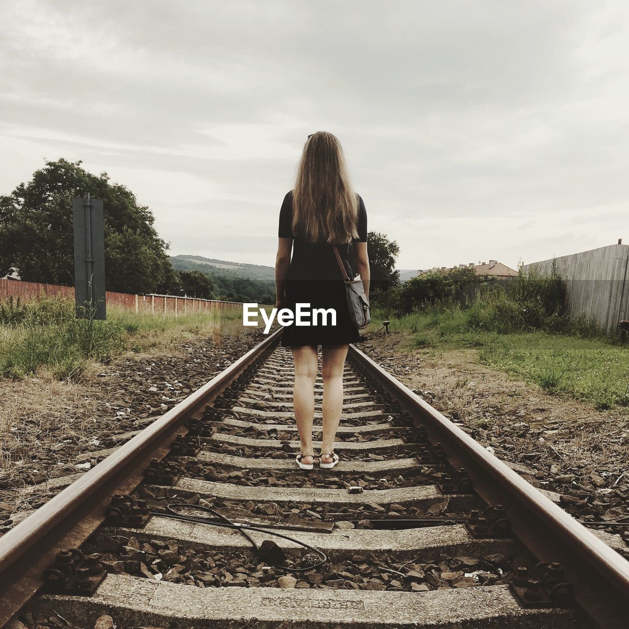 Rear view of woman standing on railway tracks against sky