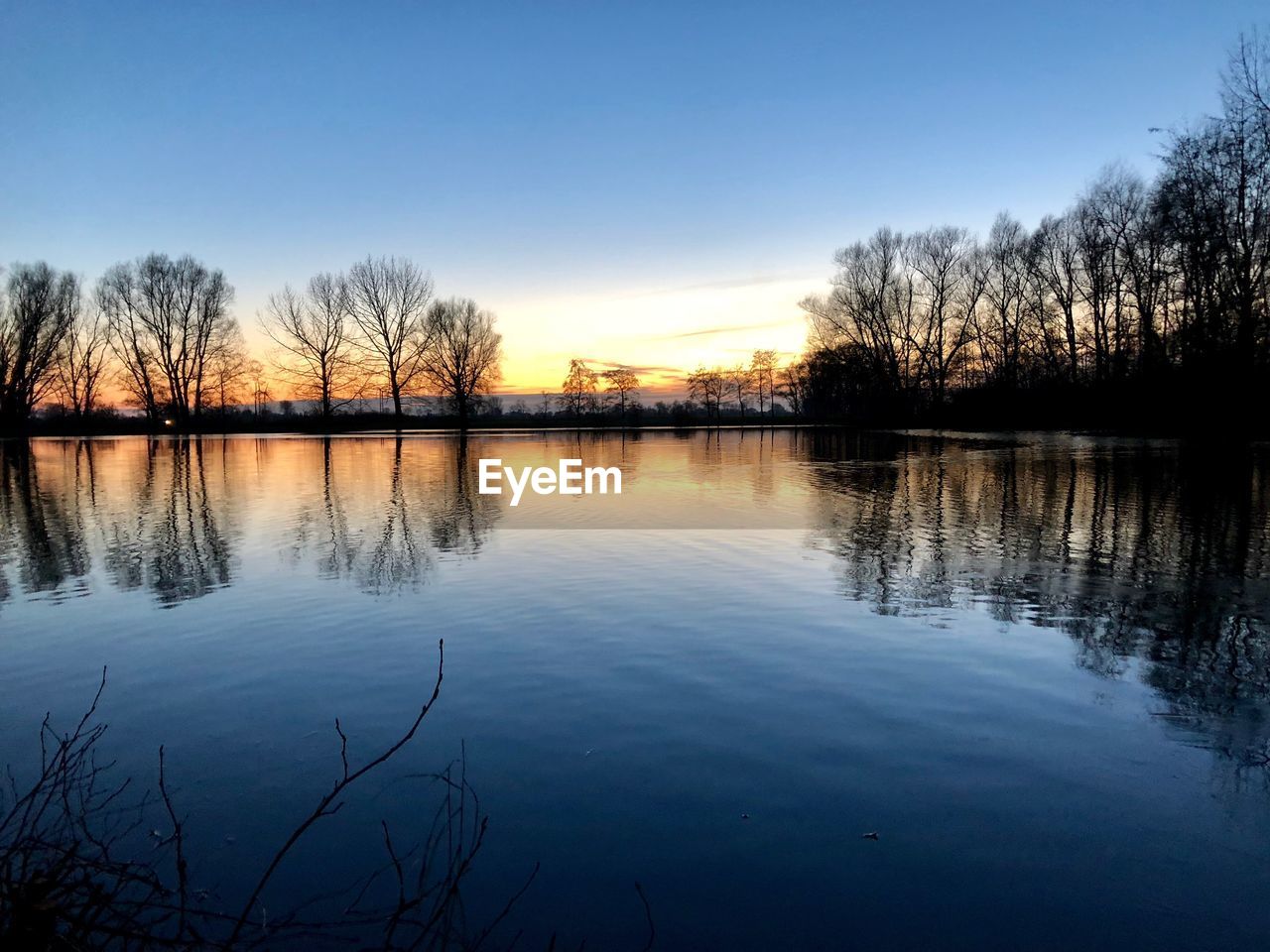 REFLECTION OF SILHOUETTE TREES IN LAKE AGAINST SKY