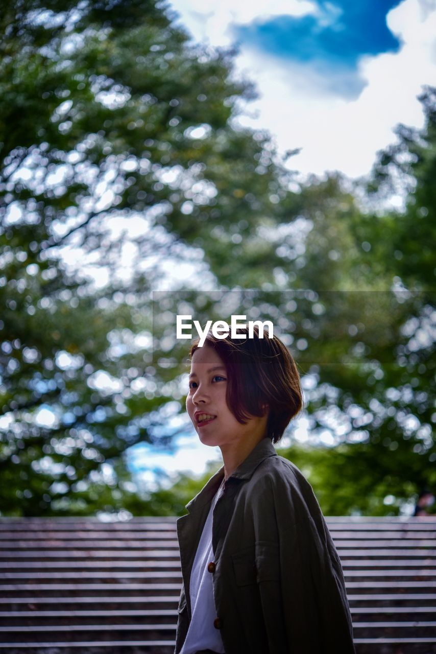 Portrait of a smiling young woman standing against trees