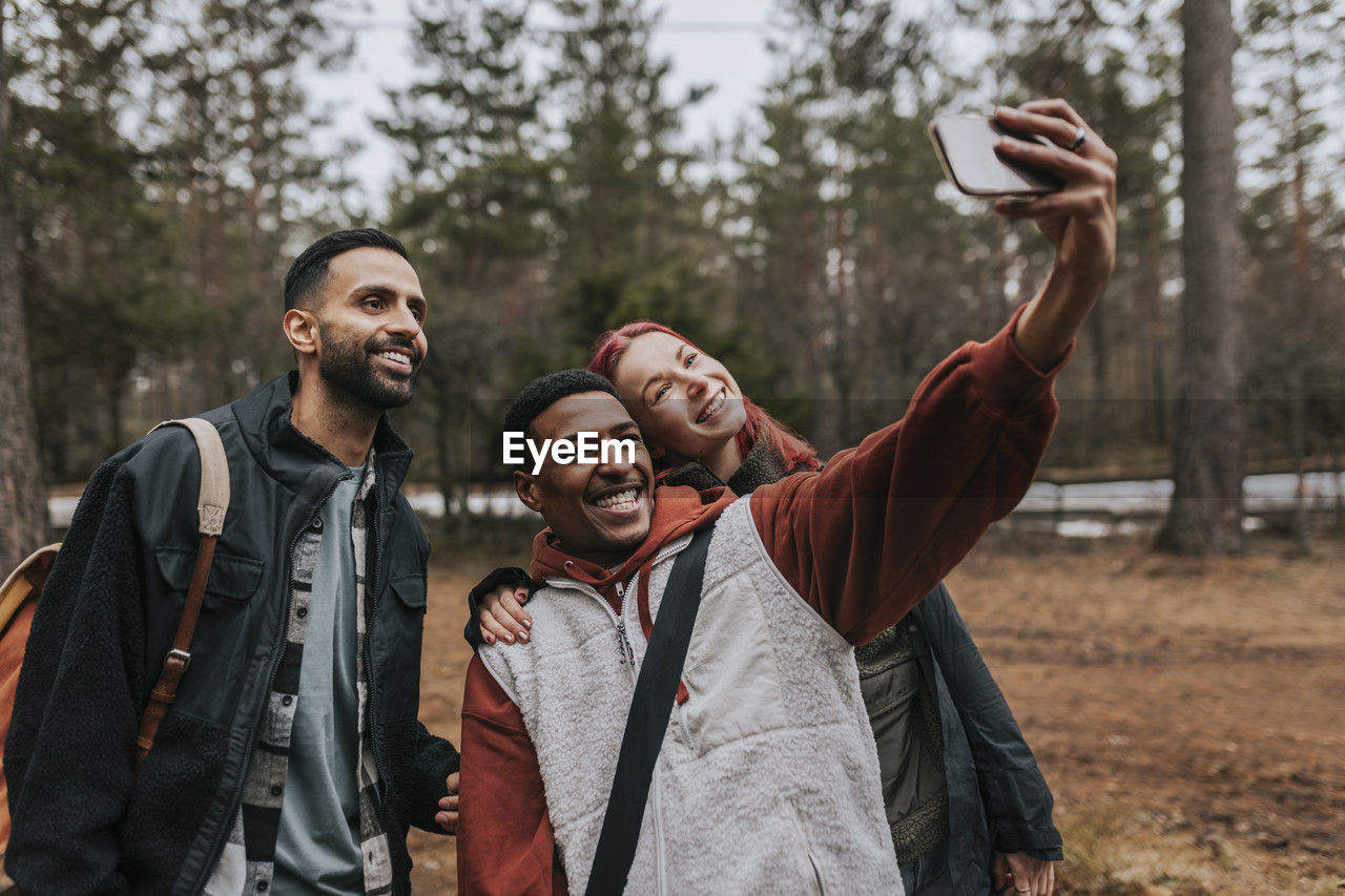 Happy multiracial friends taking selfie with smart phone in yard