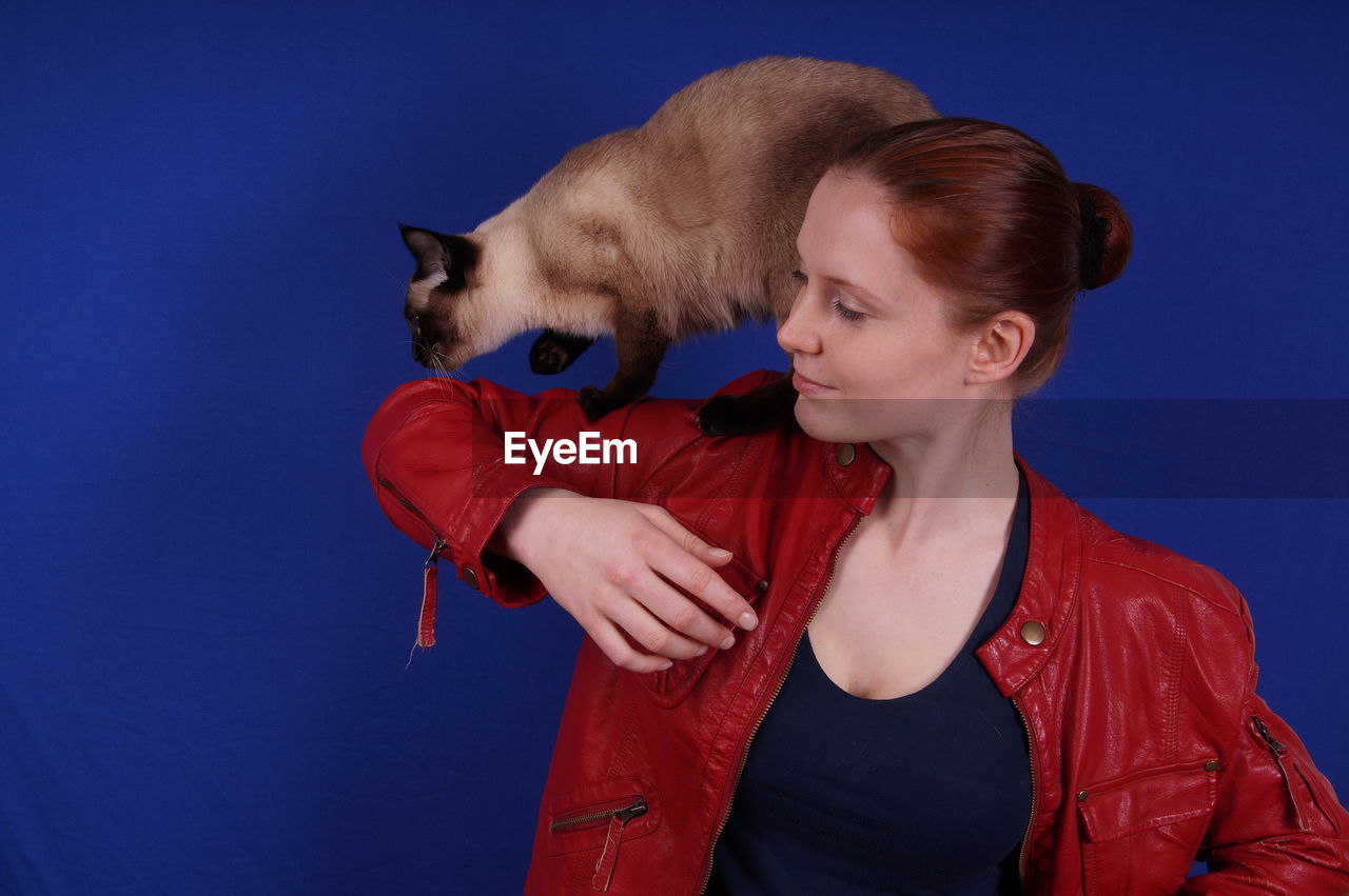 Young woman carrying cat while standing against blue background