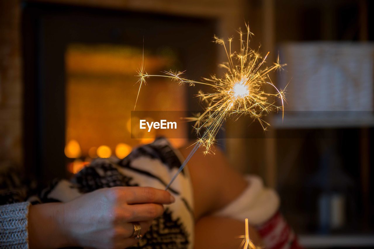 Cropped hand of woman holding lit sparkler in darkroom