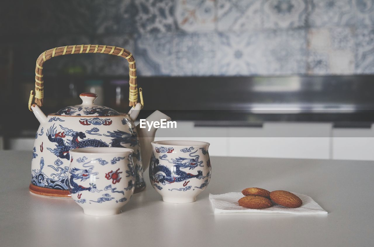 Close-up of crockery by biscuits on table in kitchen