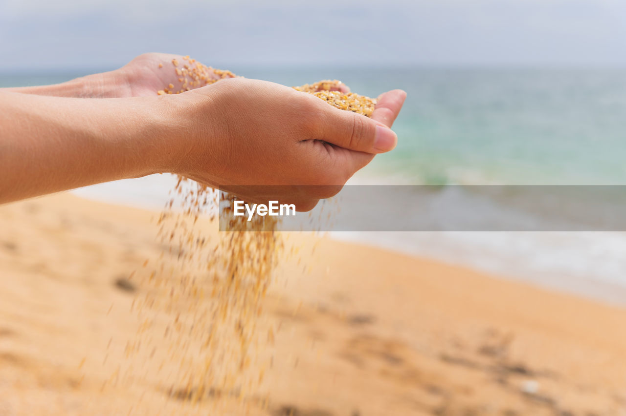 The hand releases the falling sand. golden sand flows through your fingers on a sea background