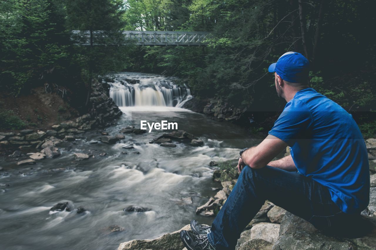 Man sitting on rock against waterfall in forest