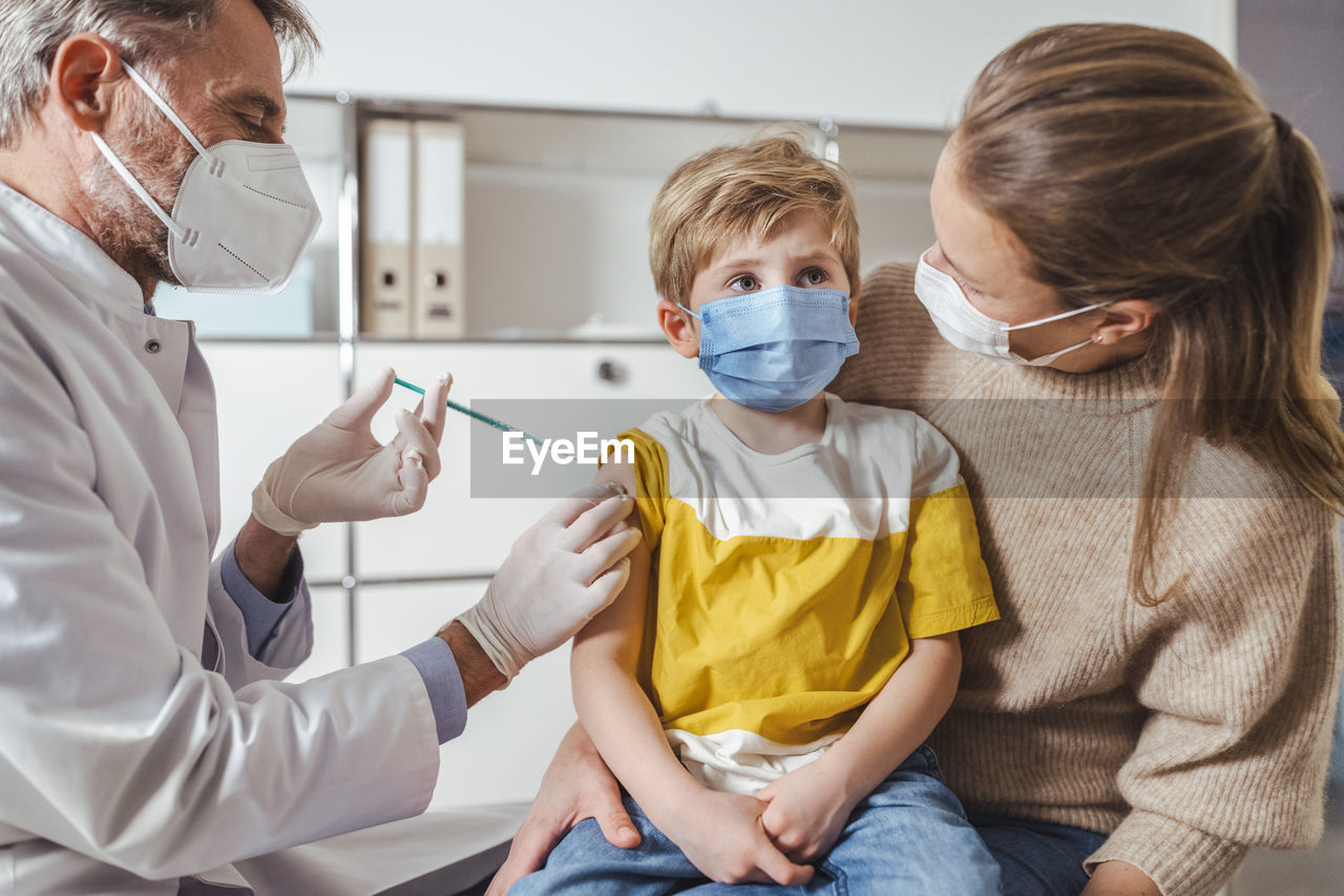 Boy being vaccinated by doctor while on lap of mother