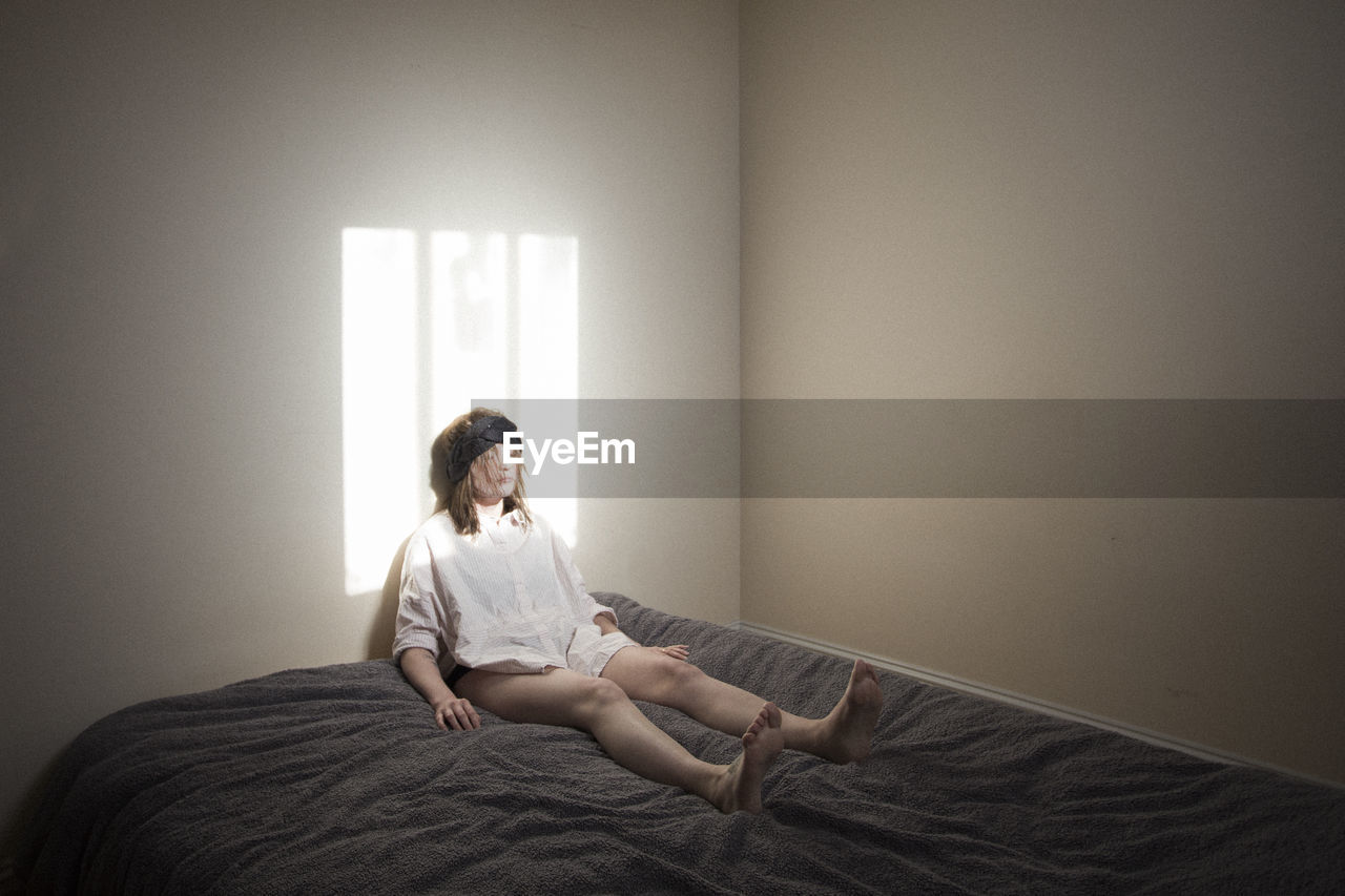 Woman sitting on bed against wall at home