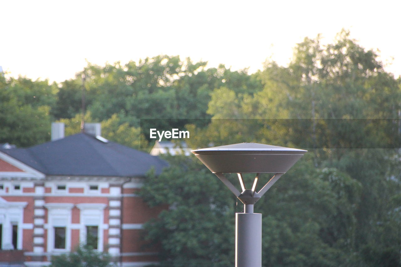 CLOSE-UP OF LAMP AGAINST TREES AND BUILDING