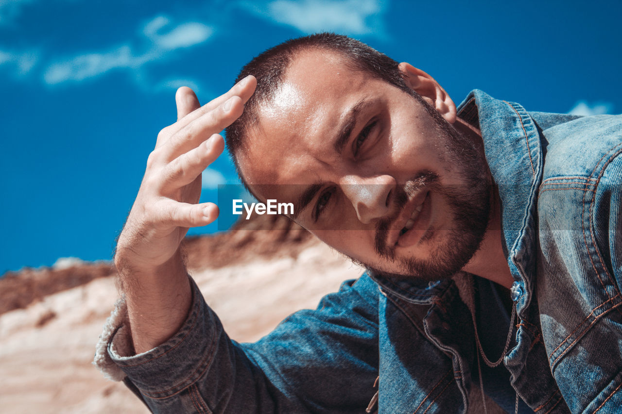 Close-up portrait of young man shielding eyes against sky