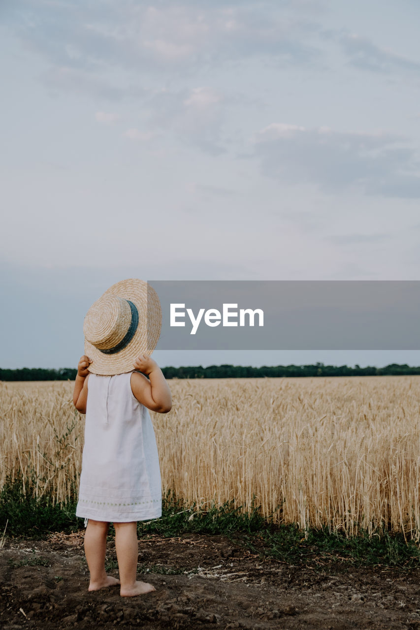 Rear view of girl wearing hat while standing on land against sky