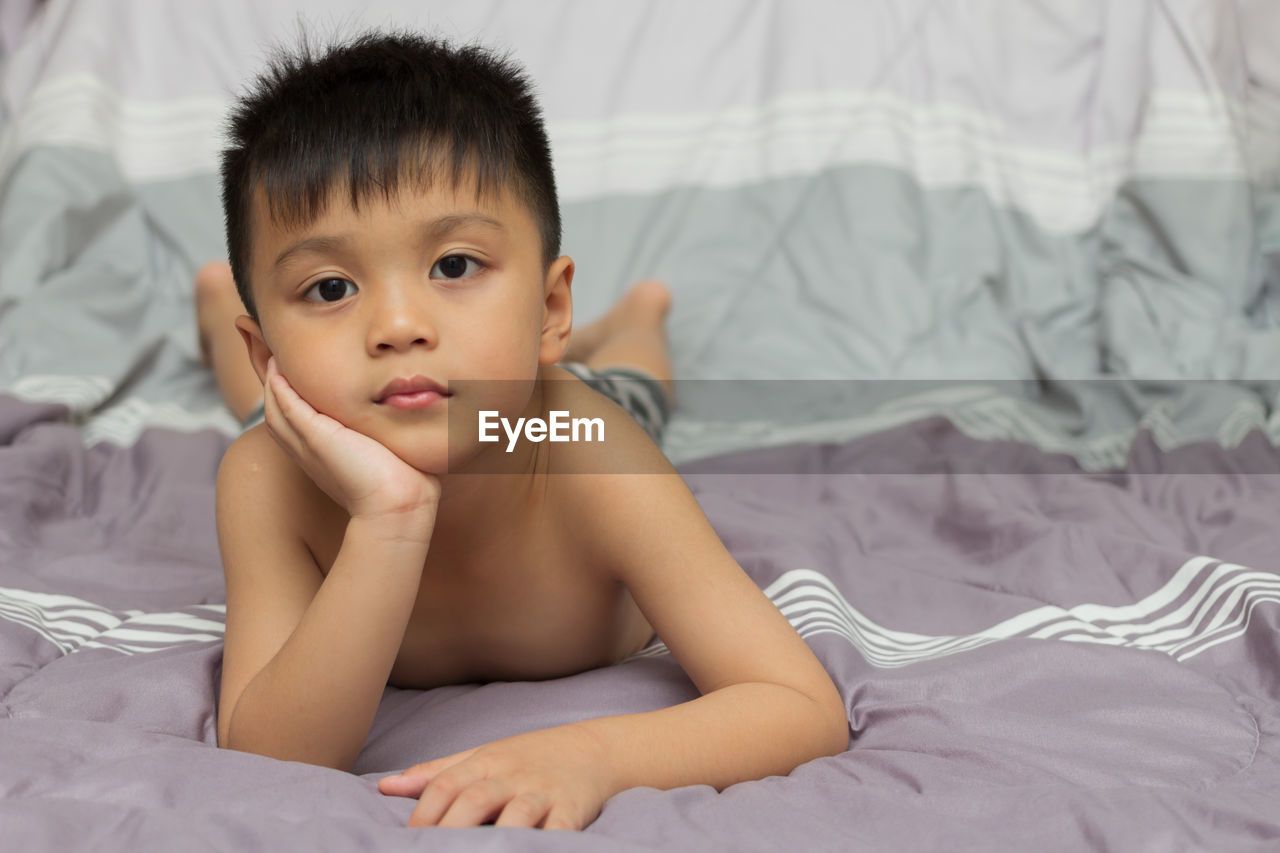 Close-up portrait of shirtless boy lying on bed at home