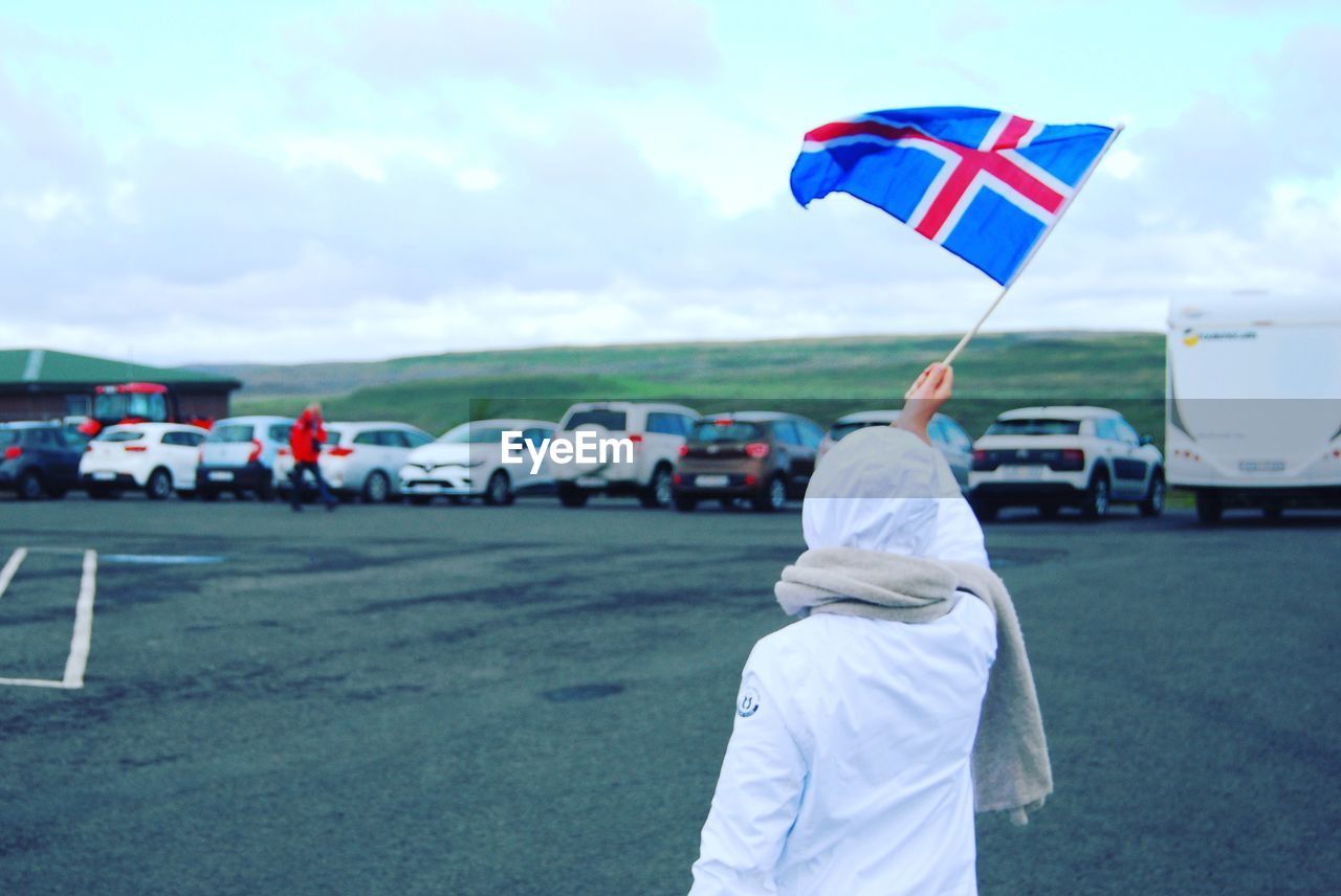 Rear view of woman holding flag while standing on road against sky