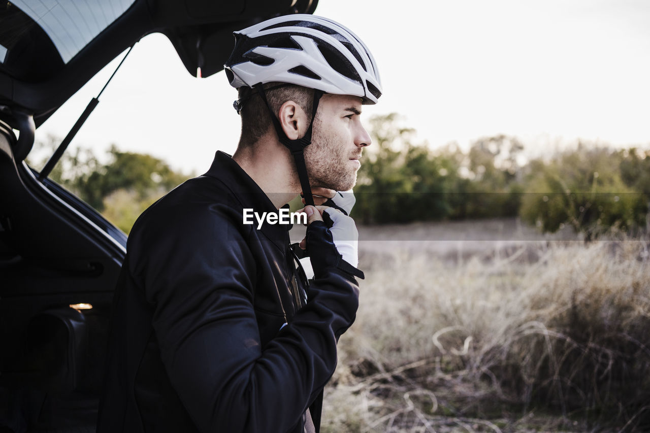 Sportsman wearing helmet at car trunk while looking away