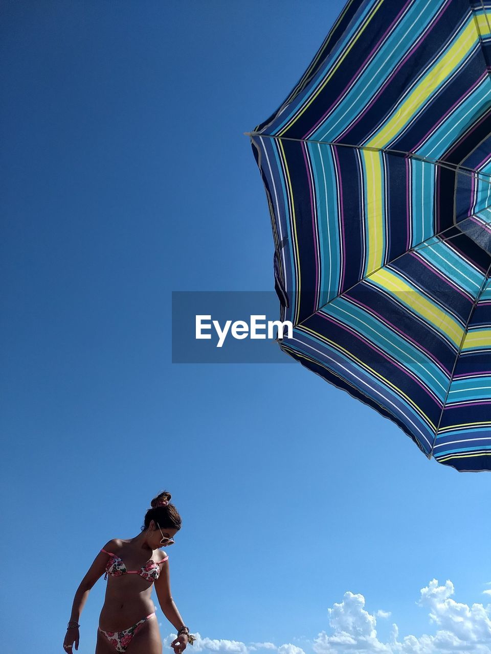 Woman standing by parasol against blue sky