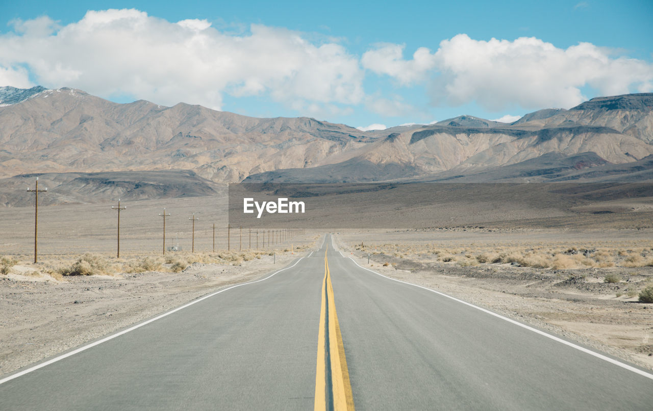 Empty road by mountains against sky