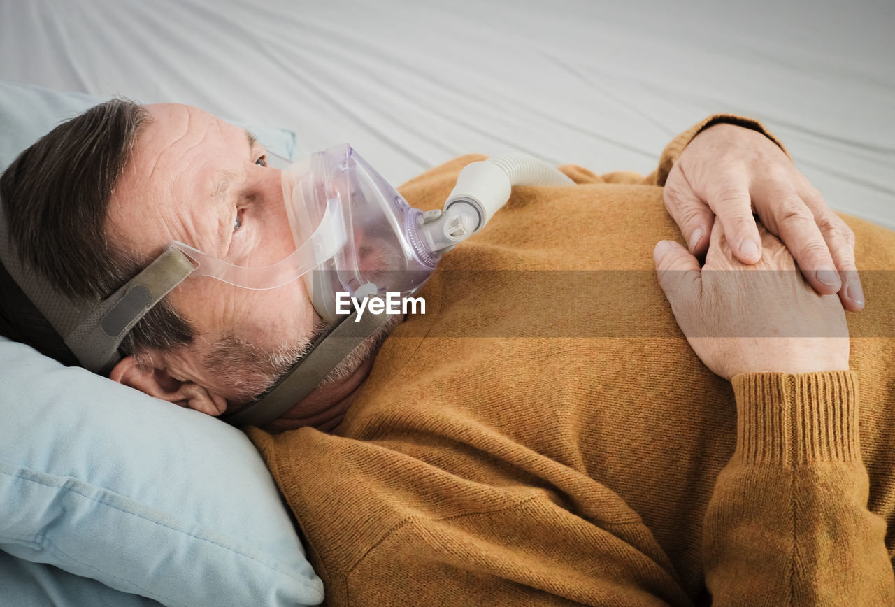 High angle view of man wearing oxygen mask while lying on bed in hospital