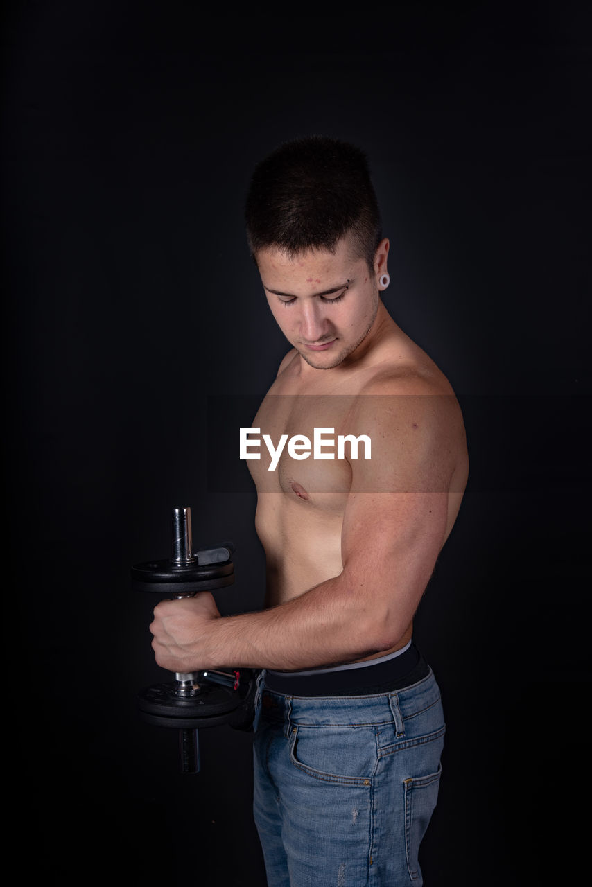 Shirtless man lifting dumbbells against black background