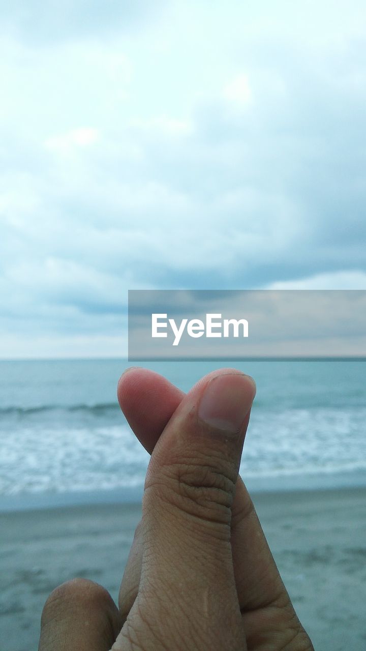 Close-up of human hand against sea