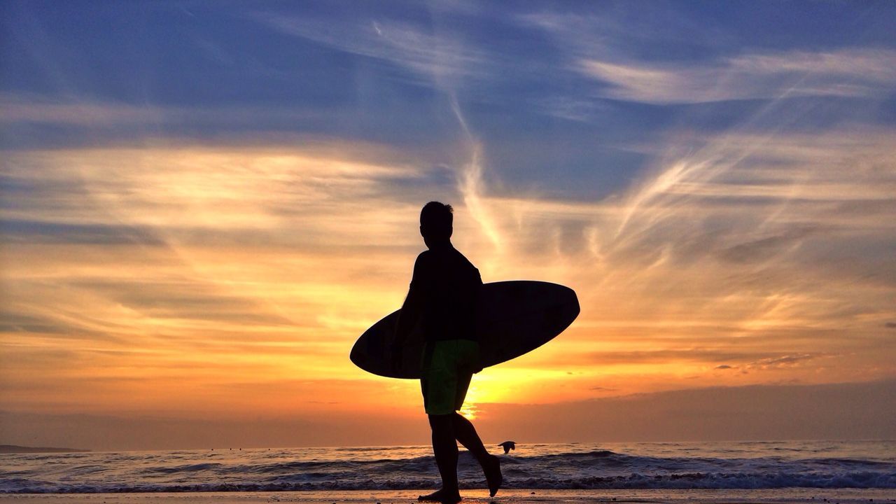 Silhouette man carrying surfboard on beach at sunset