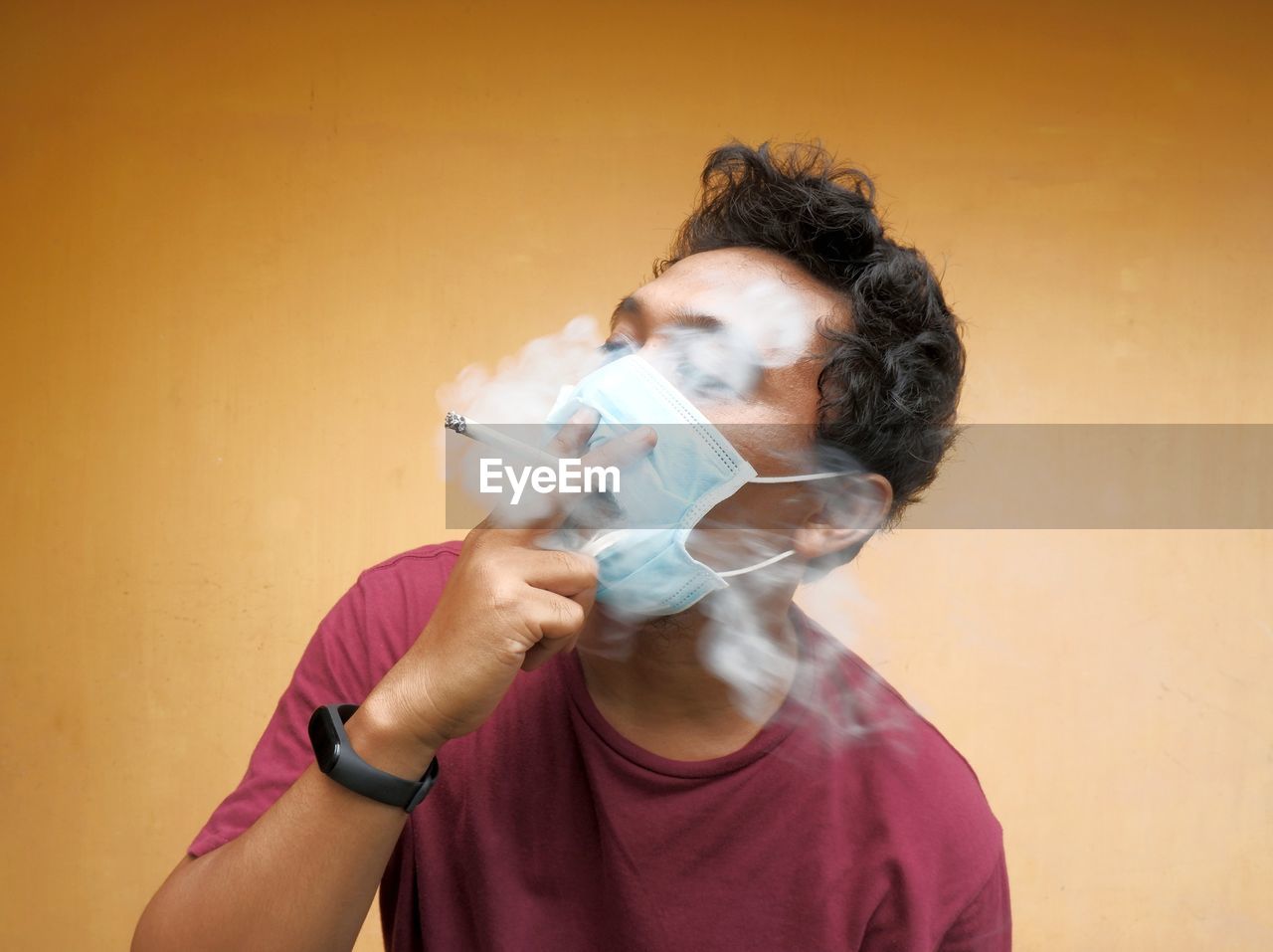 Portait of young man smoking and wearing face mask