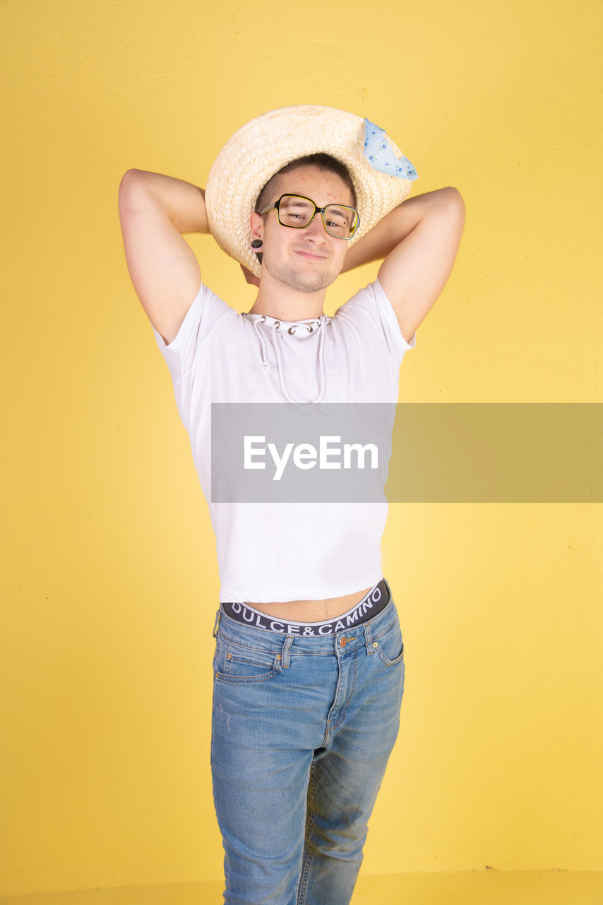 Portrait of smiling young man wearing hat standing against yellow background