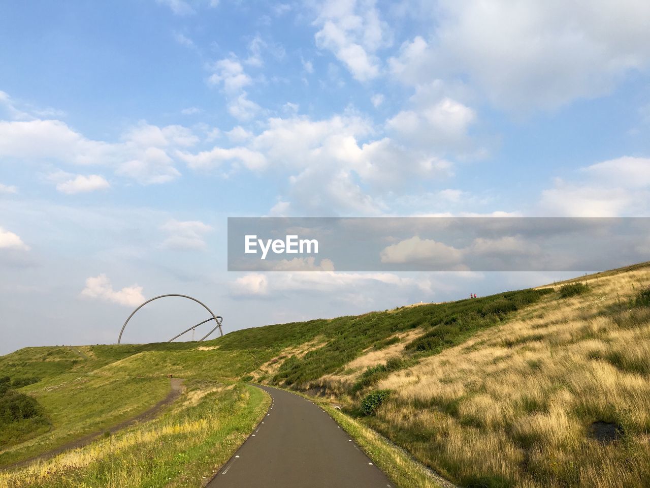 Empty road by grassy hill against sky