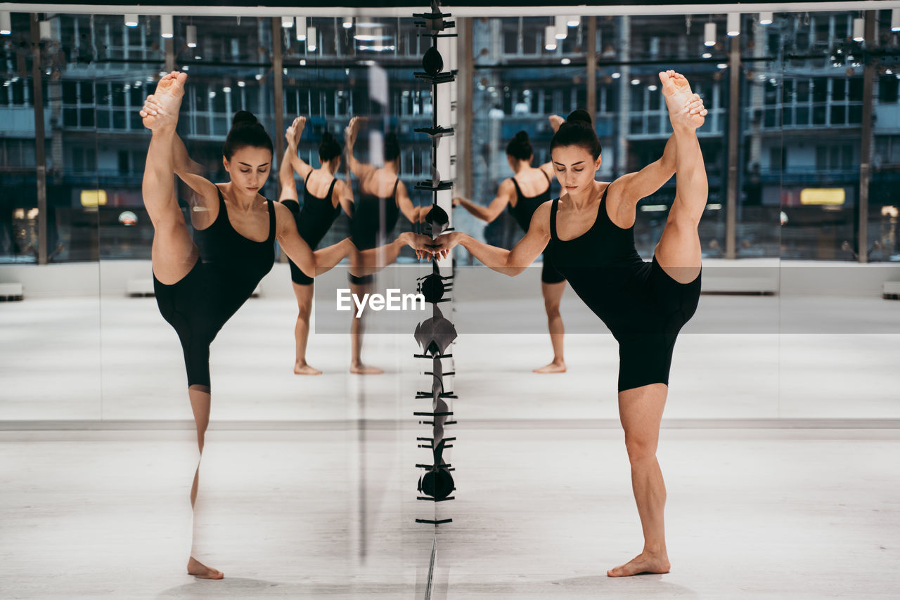 Full length of woman stretching while standing by mirror at gym